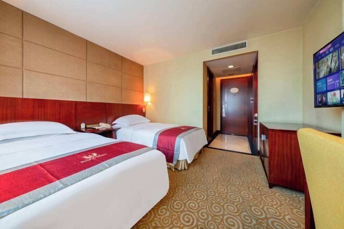 Une chambre d’hôtel avec deux lits, un bureau, une chaise, une télévision et une moquette à motifs.