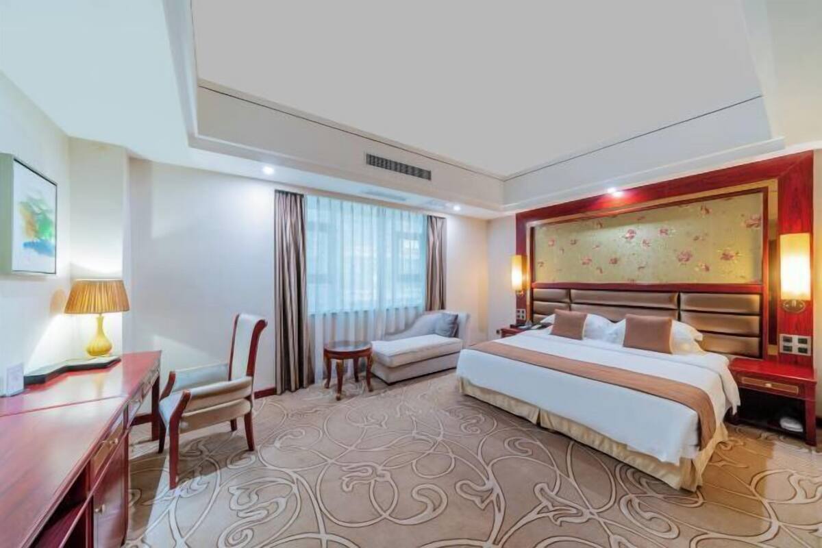 Une chambre d’hôtel avec un grand lit, un bureau, une chaise, un canapé et une fenêtre avec des rideaux.