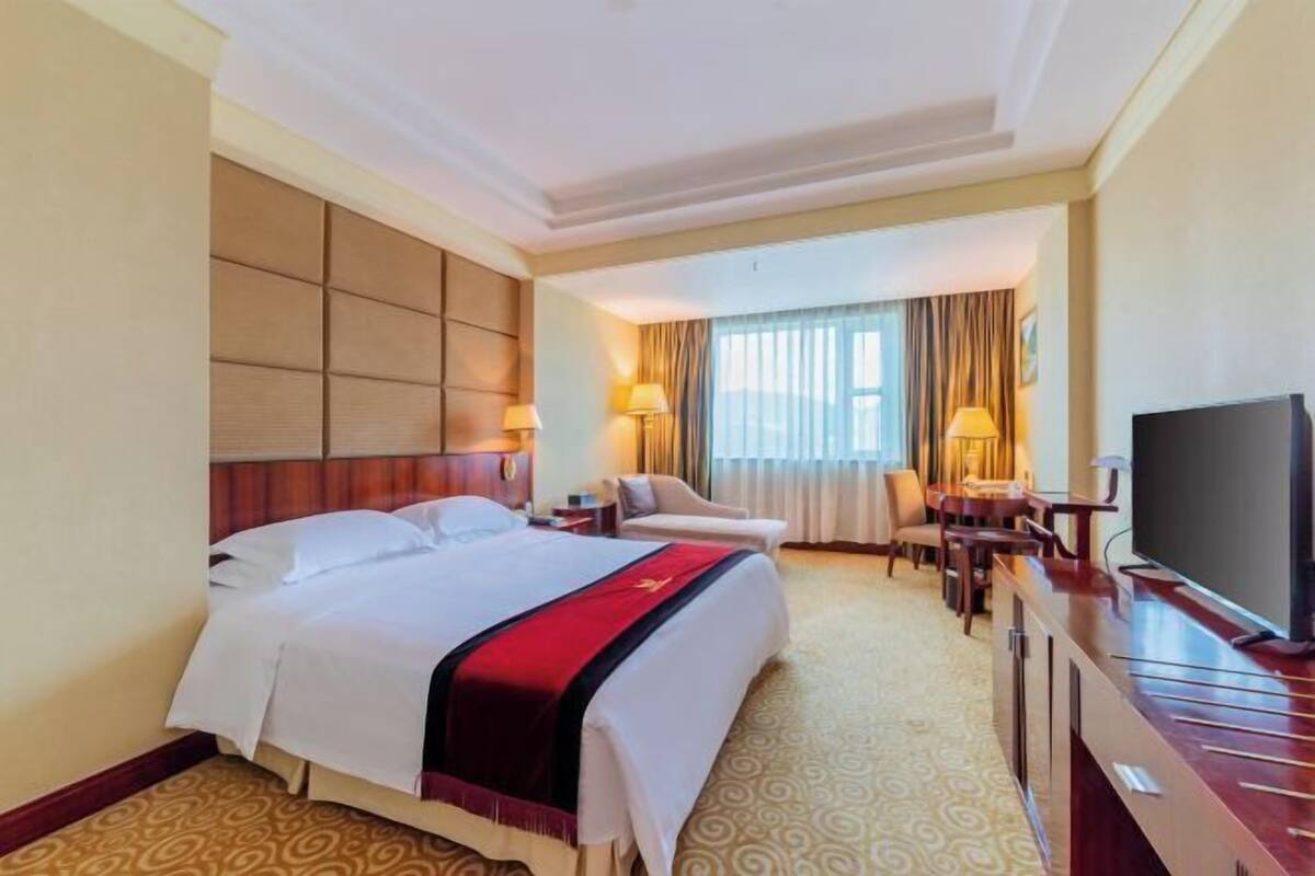 Une chambre d’hôtel avec un grand lit, un bureau doté d’un téléviseur à écran plat, deux chaises, un canapé et une fenêtre avec des rideaux.