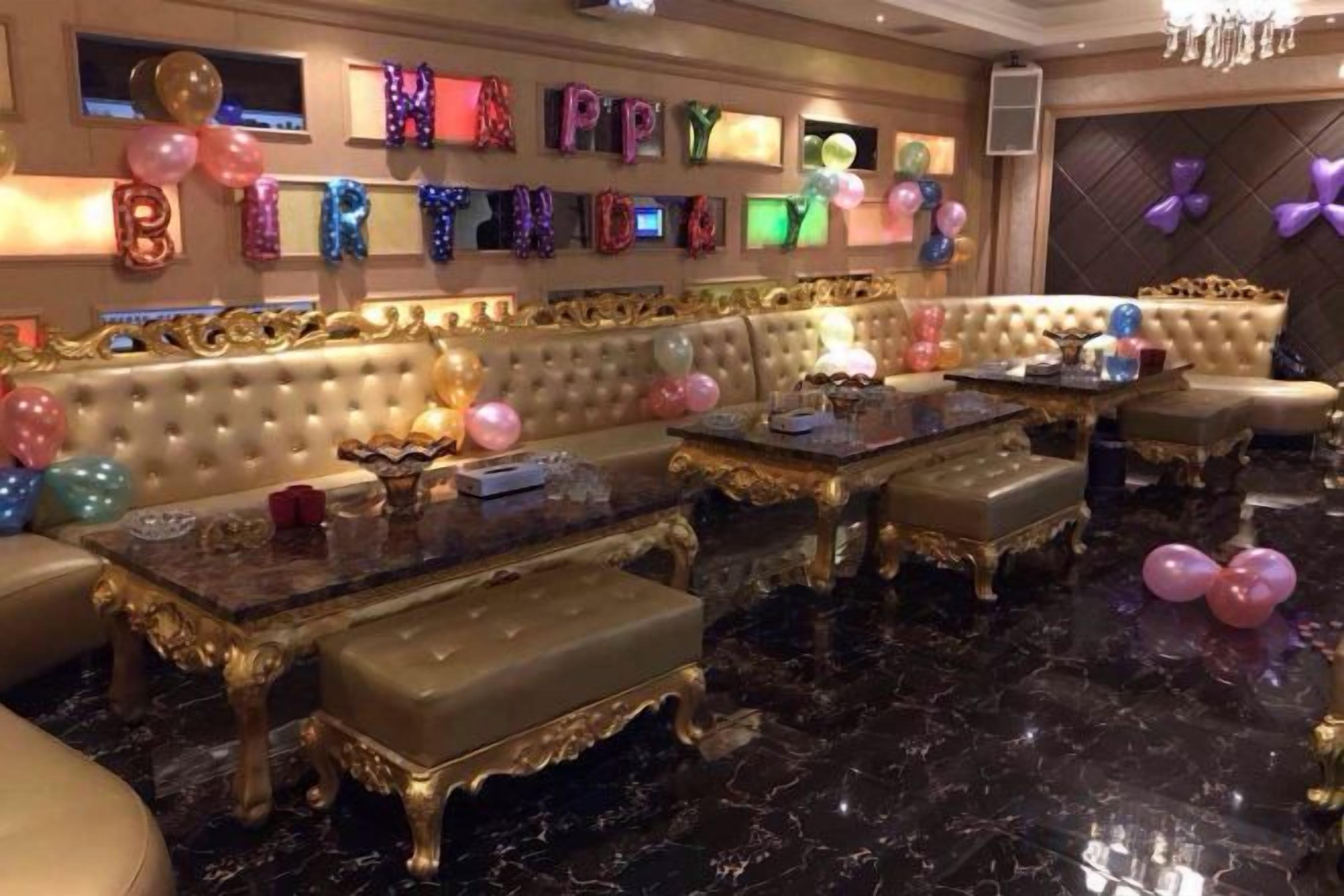 A luxurious lounge area with a plush sofa, ornate coffee tables, and a wall decorated with balloons and a 'Happy Birthday' sign.