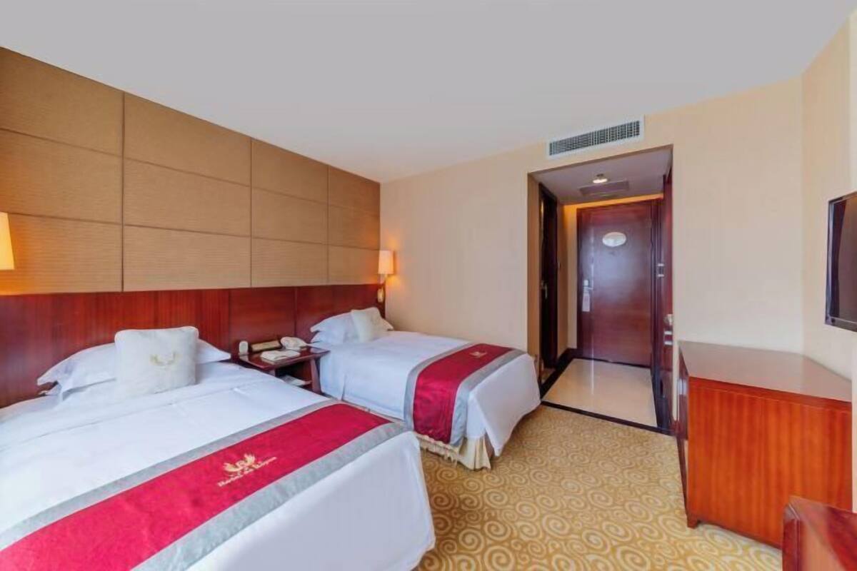 Une chambre d’hôtel avec deux lits, une tête de lit en bois, un bureau et un téléviseur.