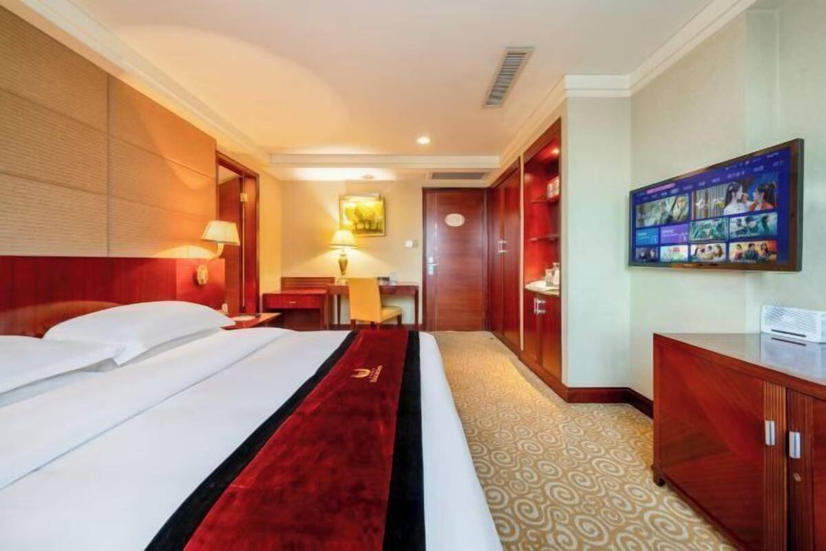 Une chambre d’hôtel avec un grand lit, un bureau, un téléviseur fixé au mur et une armoire.