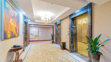 A hotel hallway with a patterned carpet, a chandelier, and a large painting on the wall.