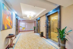 A hotel hallway with a patterned carpet, a chandelier, and a large painting on the wall. - Hotel de Royce (Shaoguan)