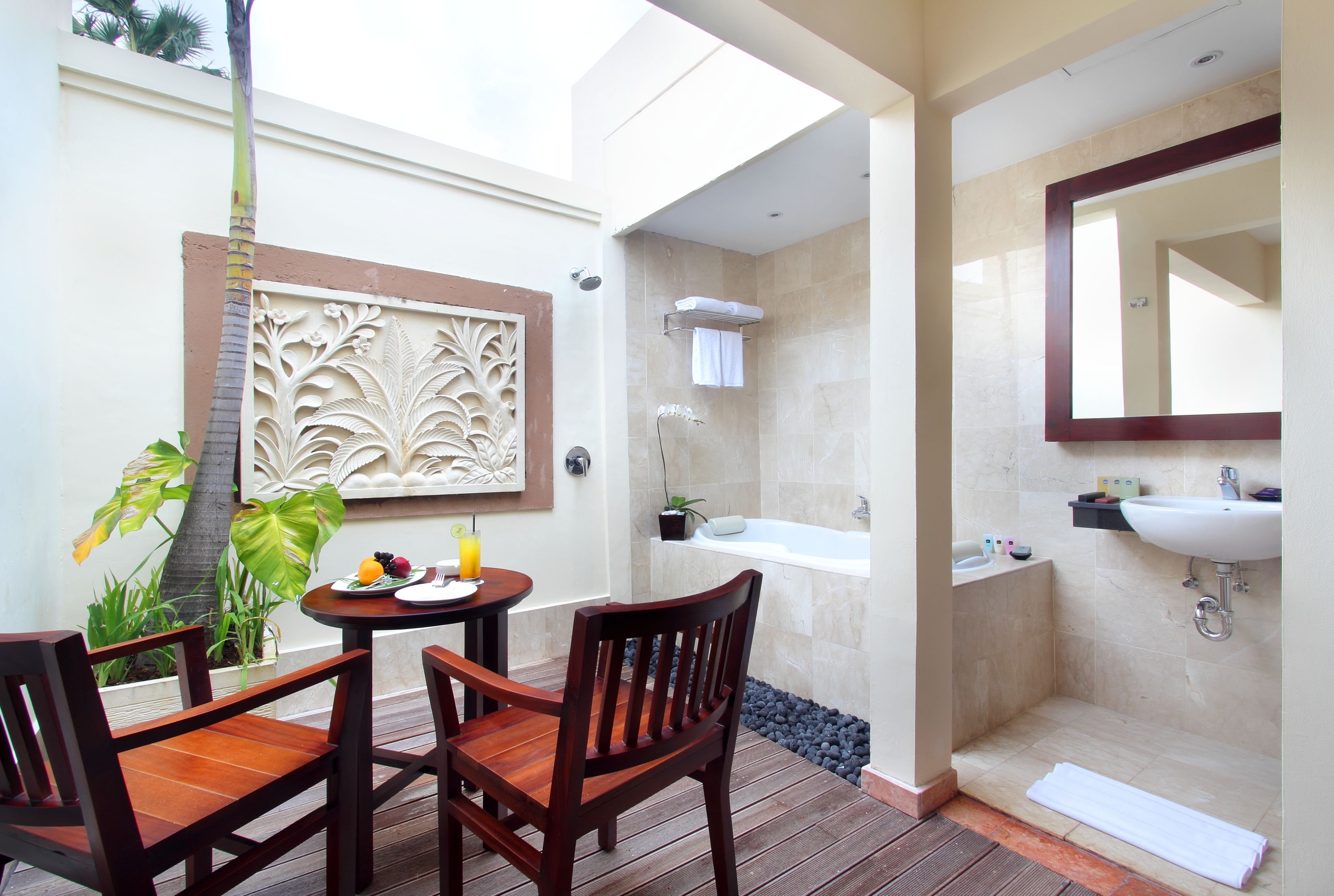 A bathroom with a bathtub, sink, and mirror. There is a table with chairs and a fruit plate.