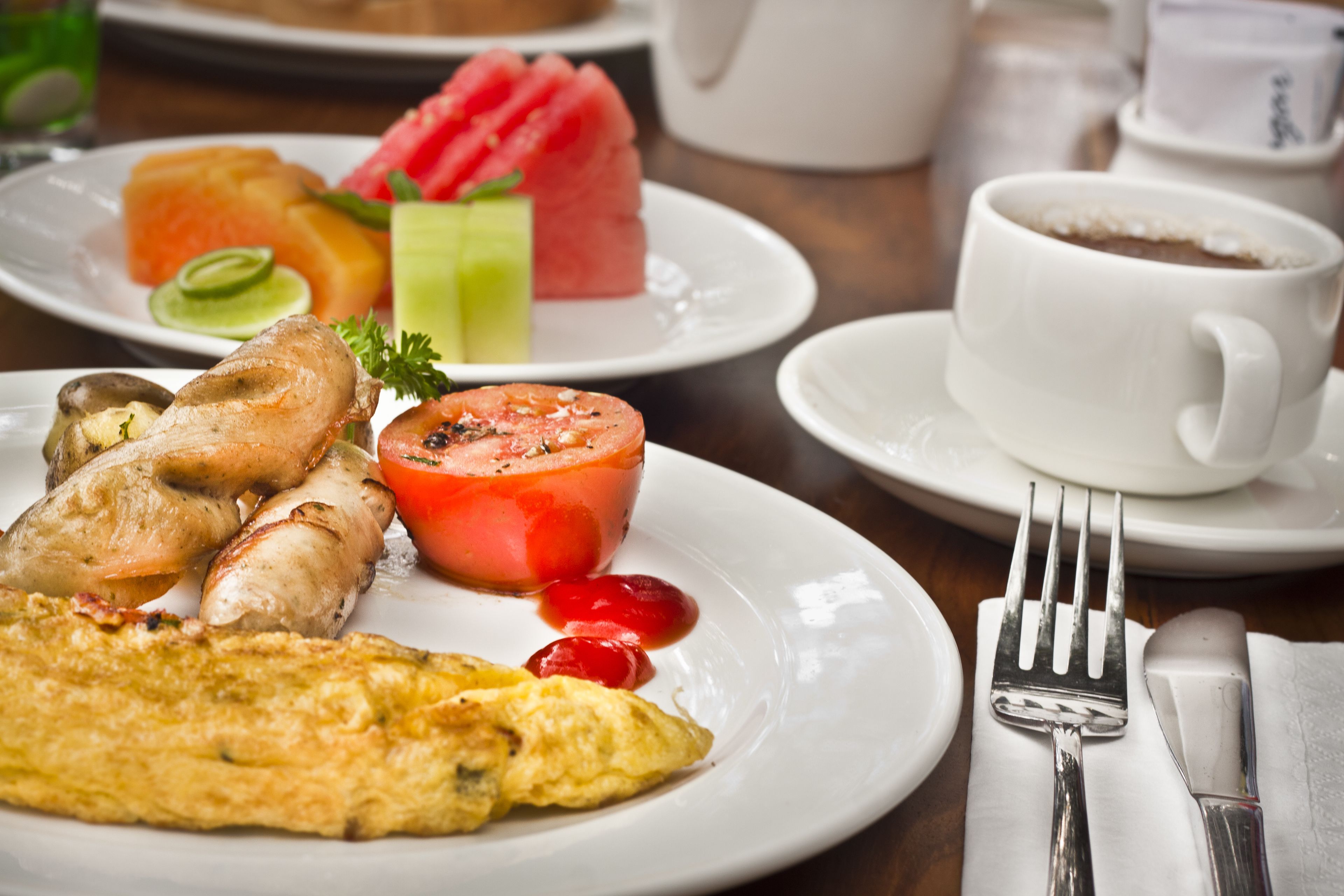 A breakfast setting with plates of food, a cup of coffee, and a fork on a table.