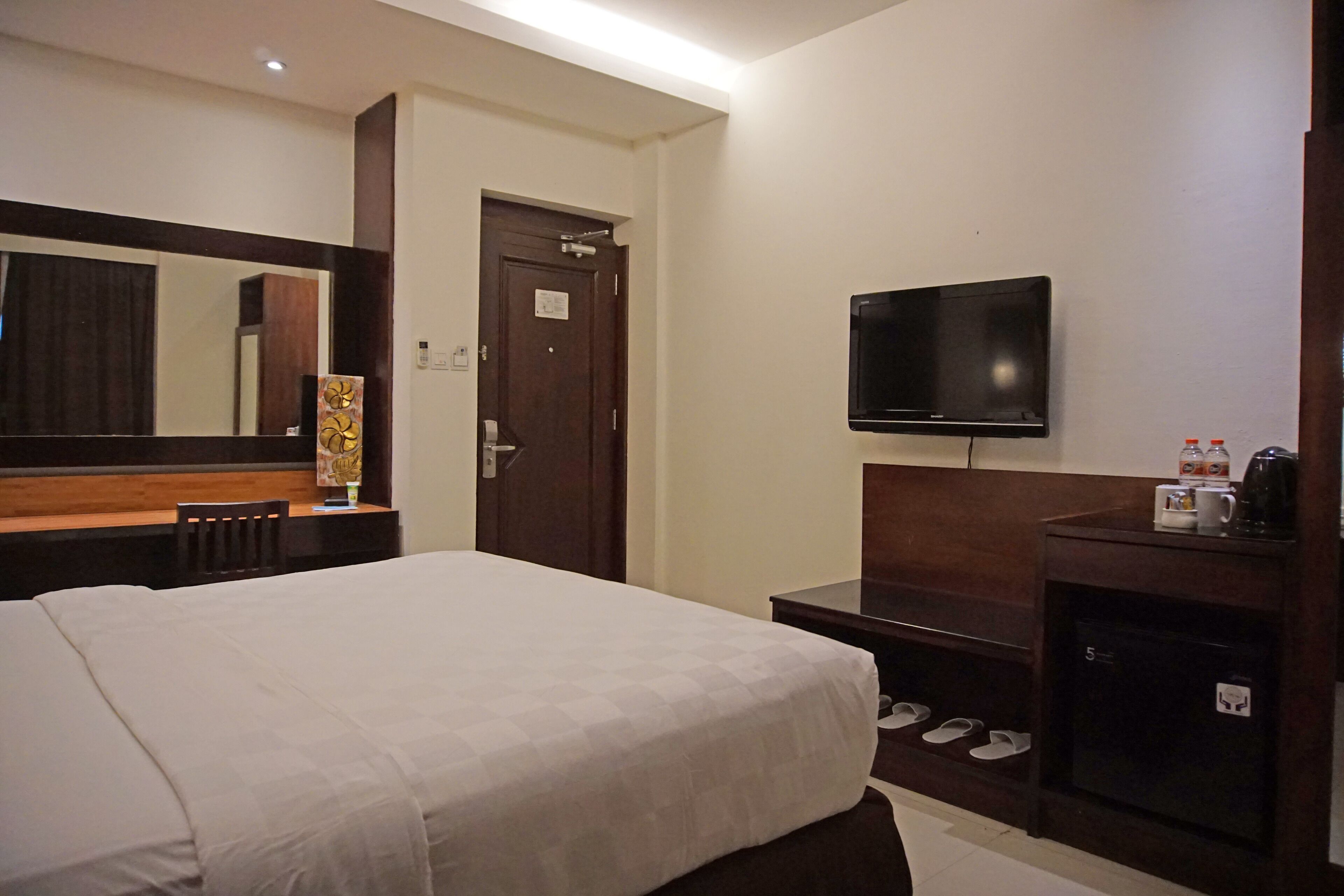 A hotel room with a bed, a TV, a desk, and a shoe storage area.