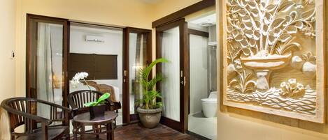 A room with a wooden floor, a dining table with chairs, a potted plant, and a decorative wall carving.