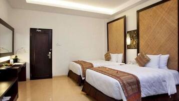 A hotel room with two beds, a dark wooden door, a small table with a lamp, and a large mirror on the wall.