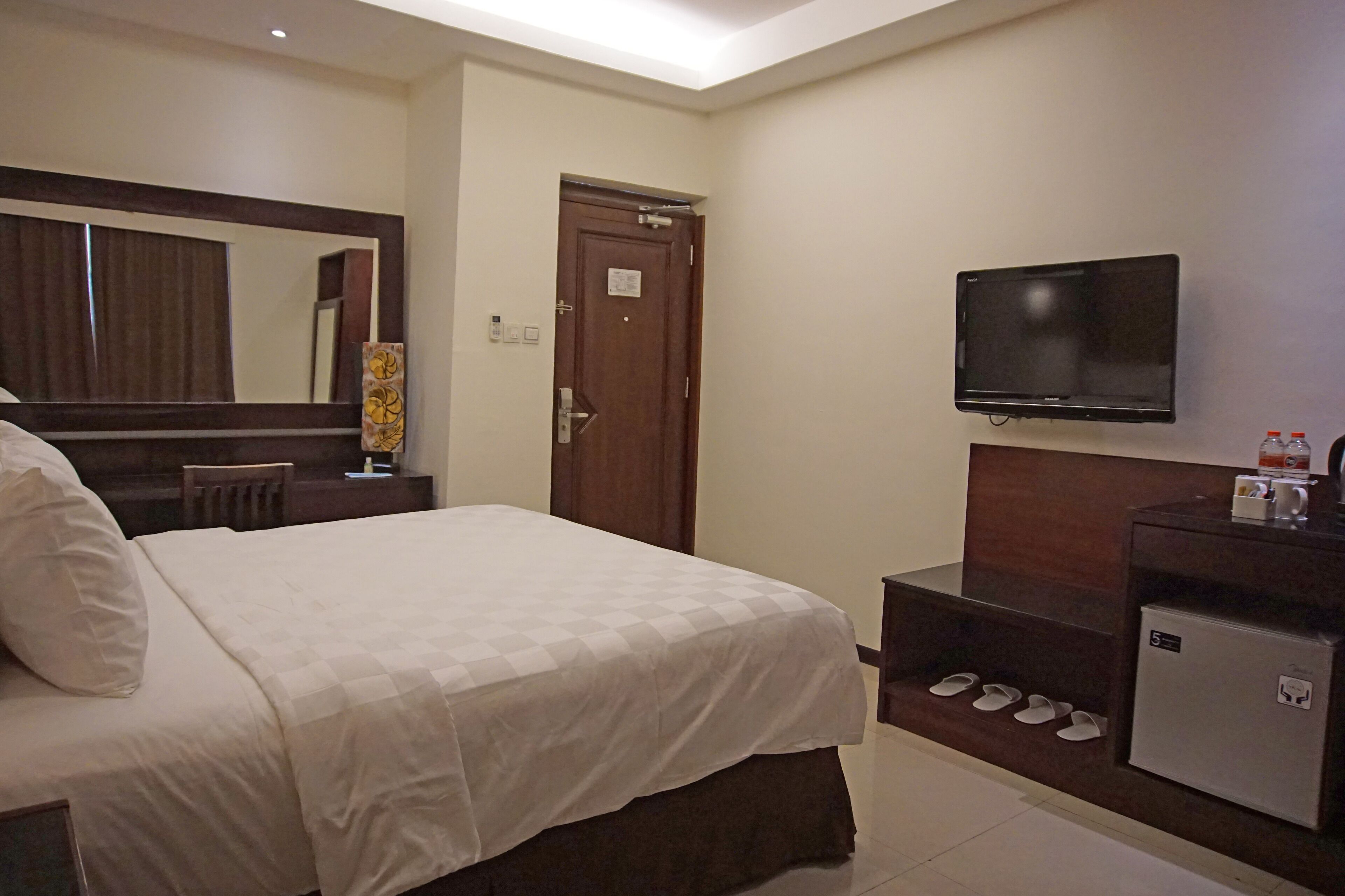 Quarto de hotel com cama, televisão, secretária com computador, espelho e porta.