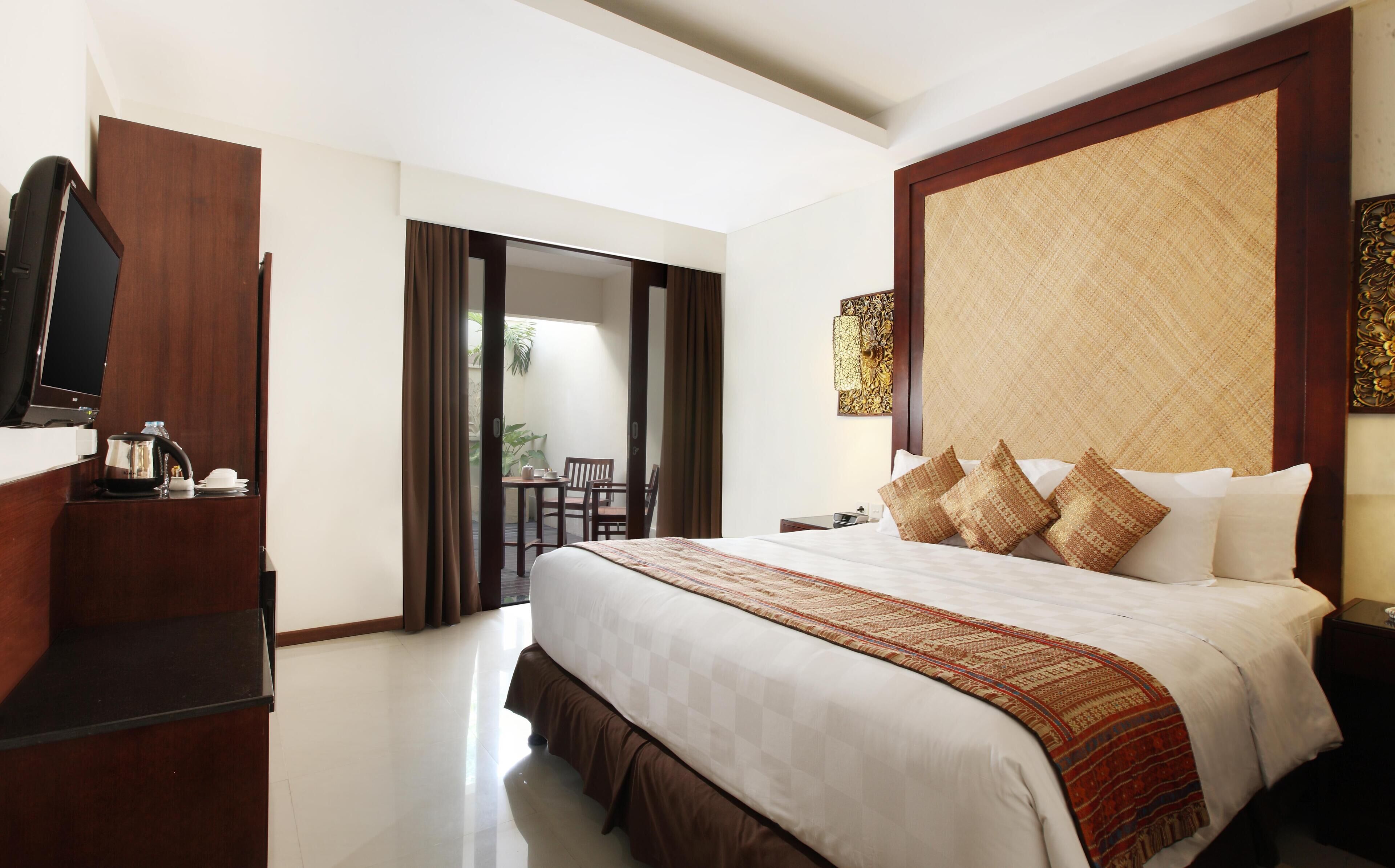 A hotel room with a large bed, a TV, a desk with a kettle, and a view of the outside balcony.