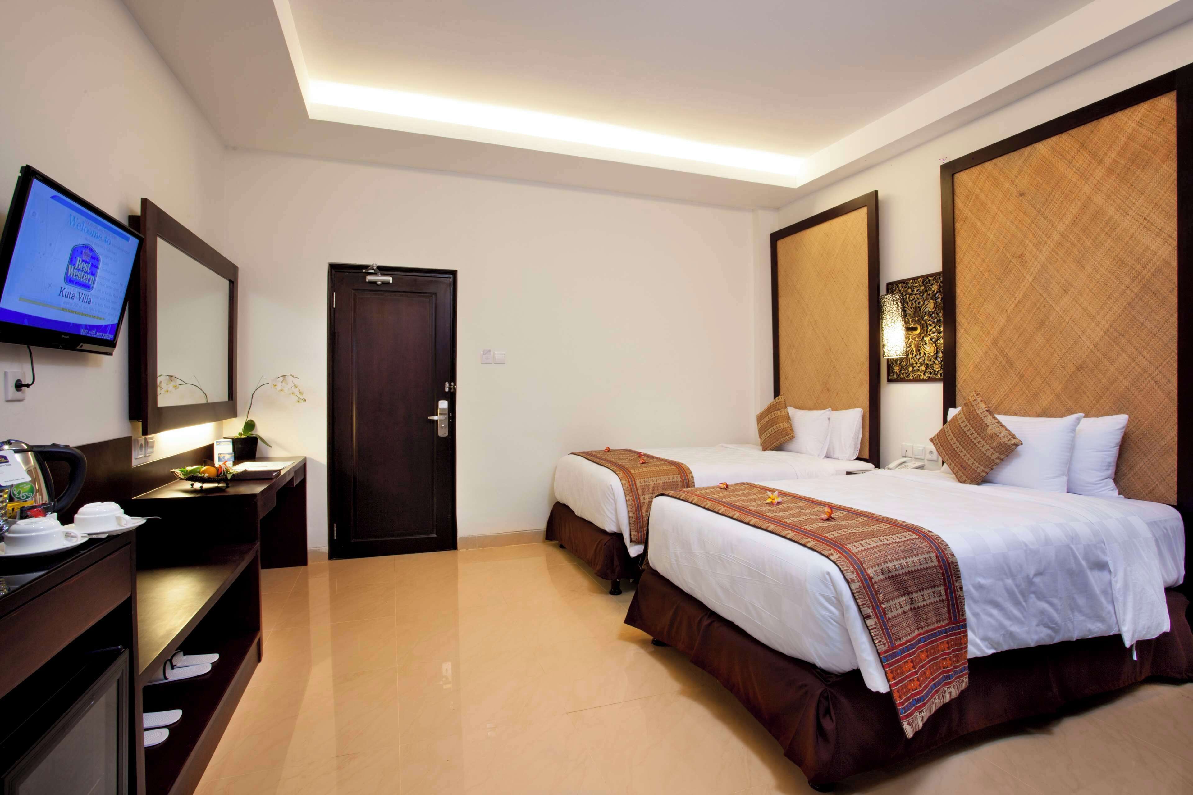 A hotel room with two beds, a desk with a computer, a TV mounted on the wall, and a door.
