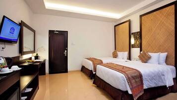 A hotel room with two beds, a desk with a computer, a TV mounted on the wall, and a door.