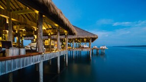 An overwater bungalows with thatched roofs, wooden pillars, and a calm sea in the background. - Song Saa Private Island (Koh Ouen)