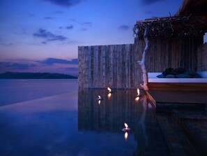 A serene infinity pool with candles, a wooden deck, and a wooden wall with a hanging vine.