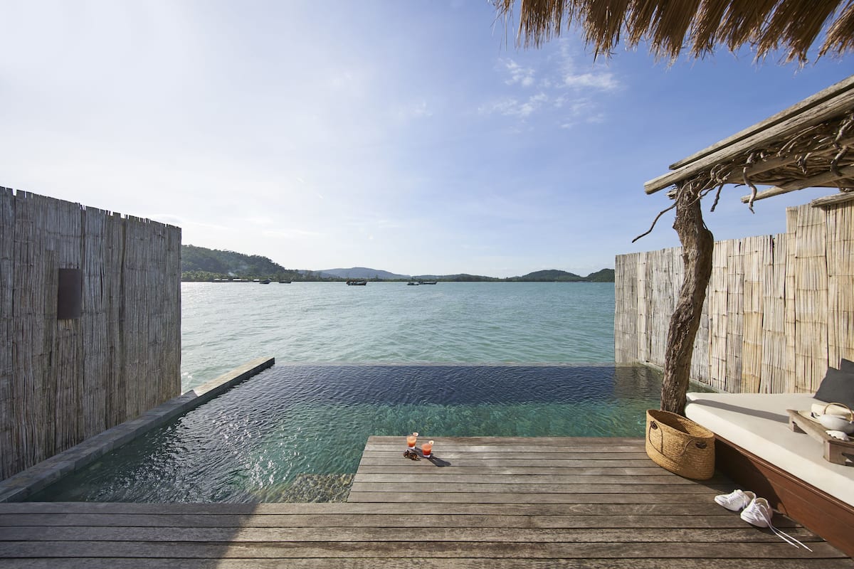 A wooden deck with a clear view of the water, a small boat, and a tree.