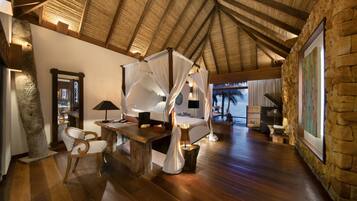 Una habitación amplia con techo alto, cama con dosel, una mesa de madera, una silla y una pared de piedra.