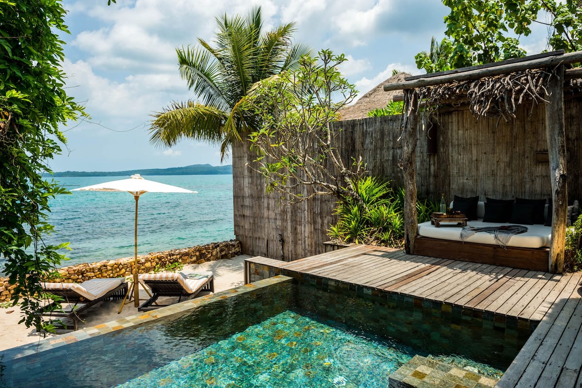 A wooden deck with a pool, lounge chairs, and a thatched-roof structure with a sofa.