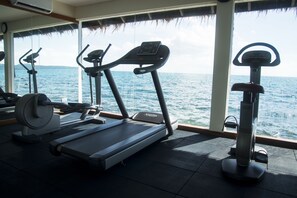 A gym with treadmills and a rowing machine, overlooking a body of water.