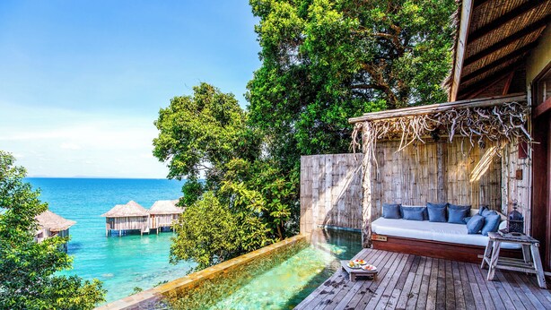 A wooden deck with a sofa and a dining table, overlooking a clear blue pool and ocean. - Song Saa Private Island (Koh Ouen)