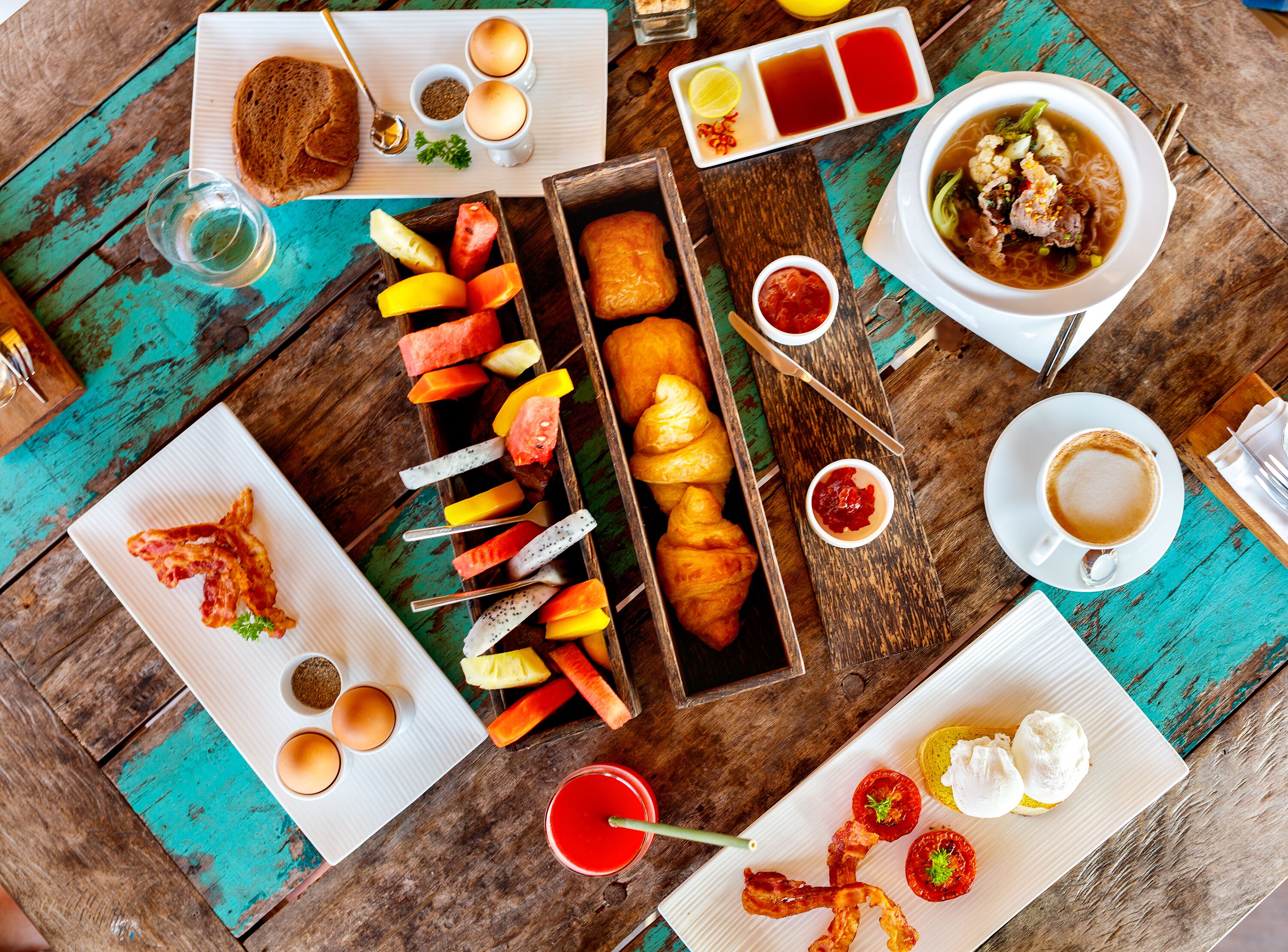 A table with various food items including croissants, fruit skewers, and a bowl of soup.