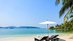 A beach with two sun loungers and a white umbrella, a clear blue sea, and palm trees in the background. - Song Saa Private Island (Koh Ouen)