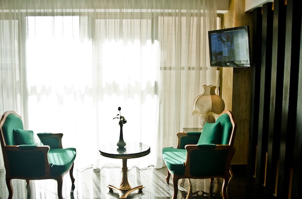A room with two green upholstered chairs, a small round table with a vase, and a television mounted on the wall.