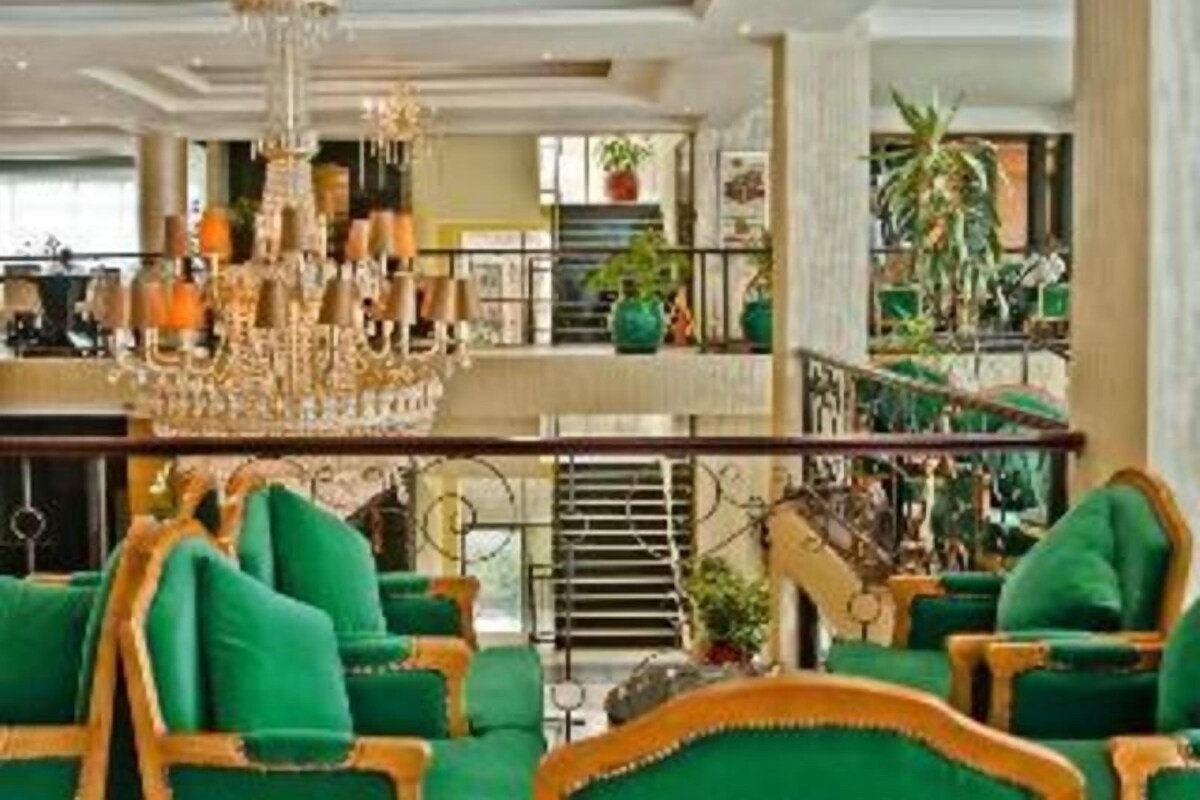 Eine Lobby mit einem Kronleuchter, grünen Polstersesseln und einer Treppe.