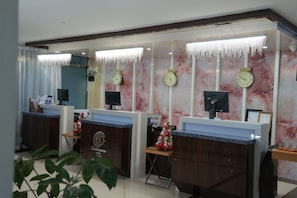 Zona de recepción con paredes de mármol, varios relojes y un mostrador de recepción.