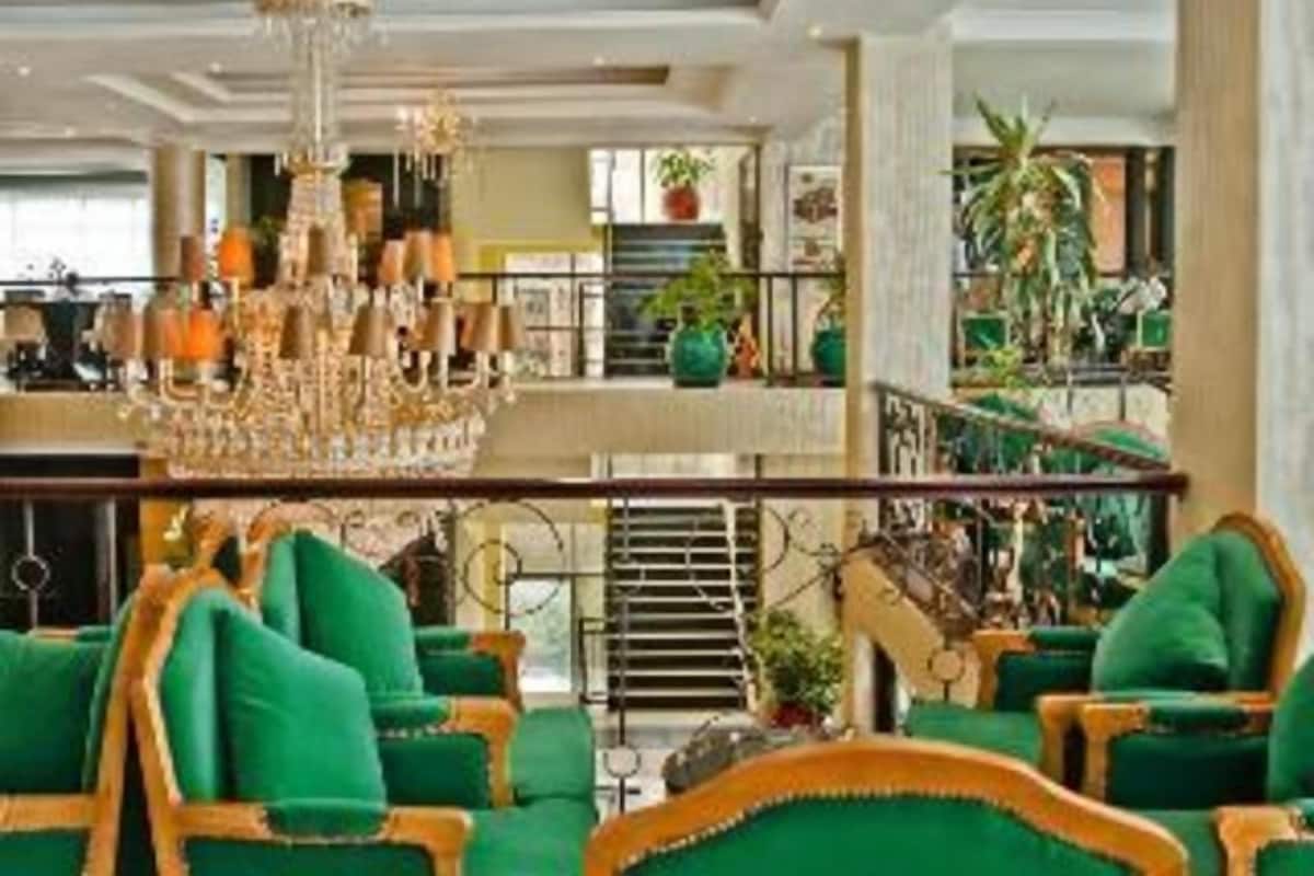 Eine Lobby mit einem Kronleuchter, grünen Polstersesseln und einer Treppe.