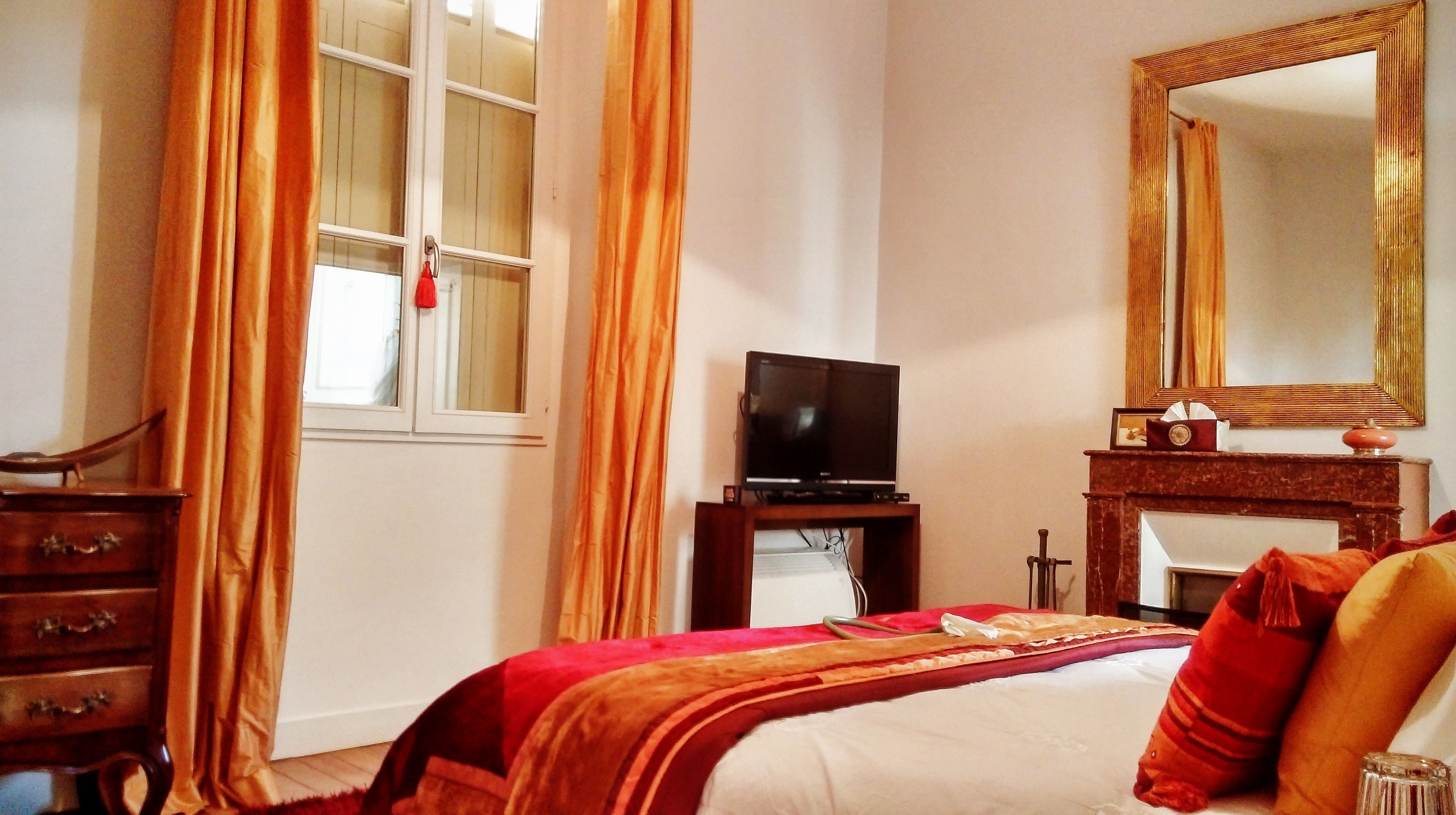 Une chambre d’hôtel avec un lit, un téléviseur posé sur un meuble, une commode, un miroir et une cheminée.