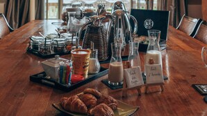 Une table de petit-déjeuner avec des viennoiseries, du café et du lait, disposée dans une pièce offrant une vue magnifique grâce à de grandes fenêtres.