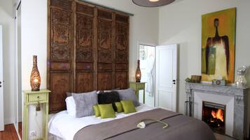 A bedroom with a large bed, a wooden headboard, a fireplace, and a painting on the wall.
