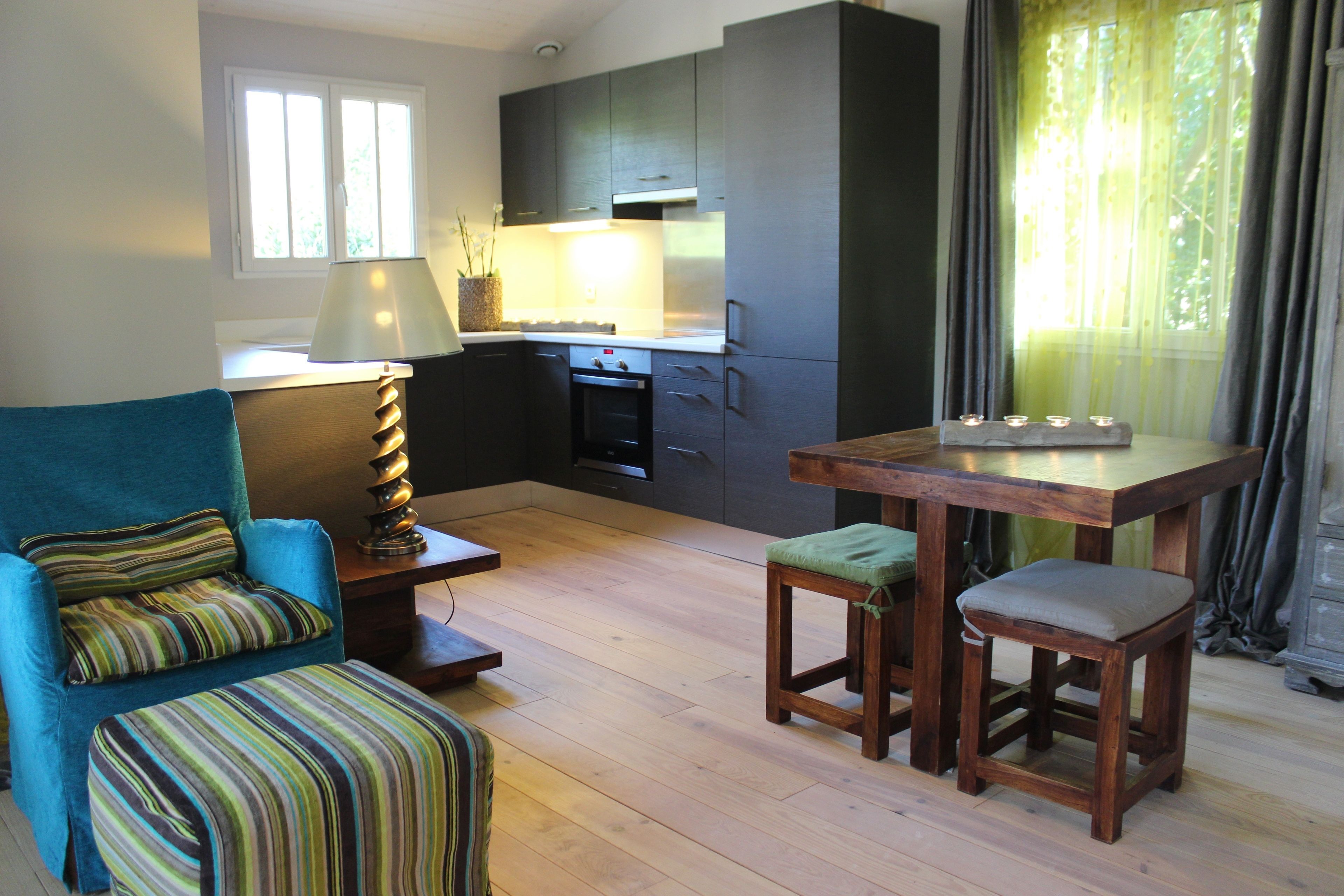 A compact living space with a kitchenette, a dining table with stools, a sofa with striped cushions, and a lamp.