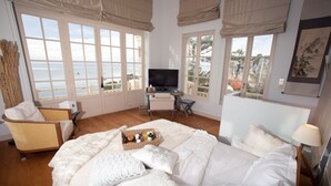 Une chambre spacieuse avec un grand lit, un bureau avec une télévision et une vue sur la mer.