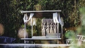 Un belvédère en bois orné d’une sculpture en relief, entouré d’une végétation luxuriante.