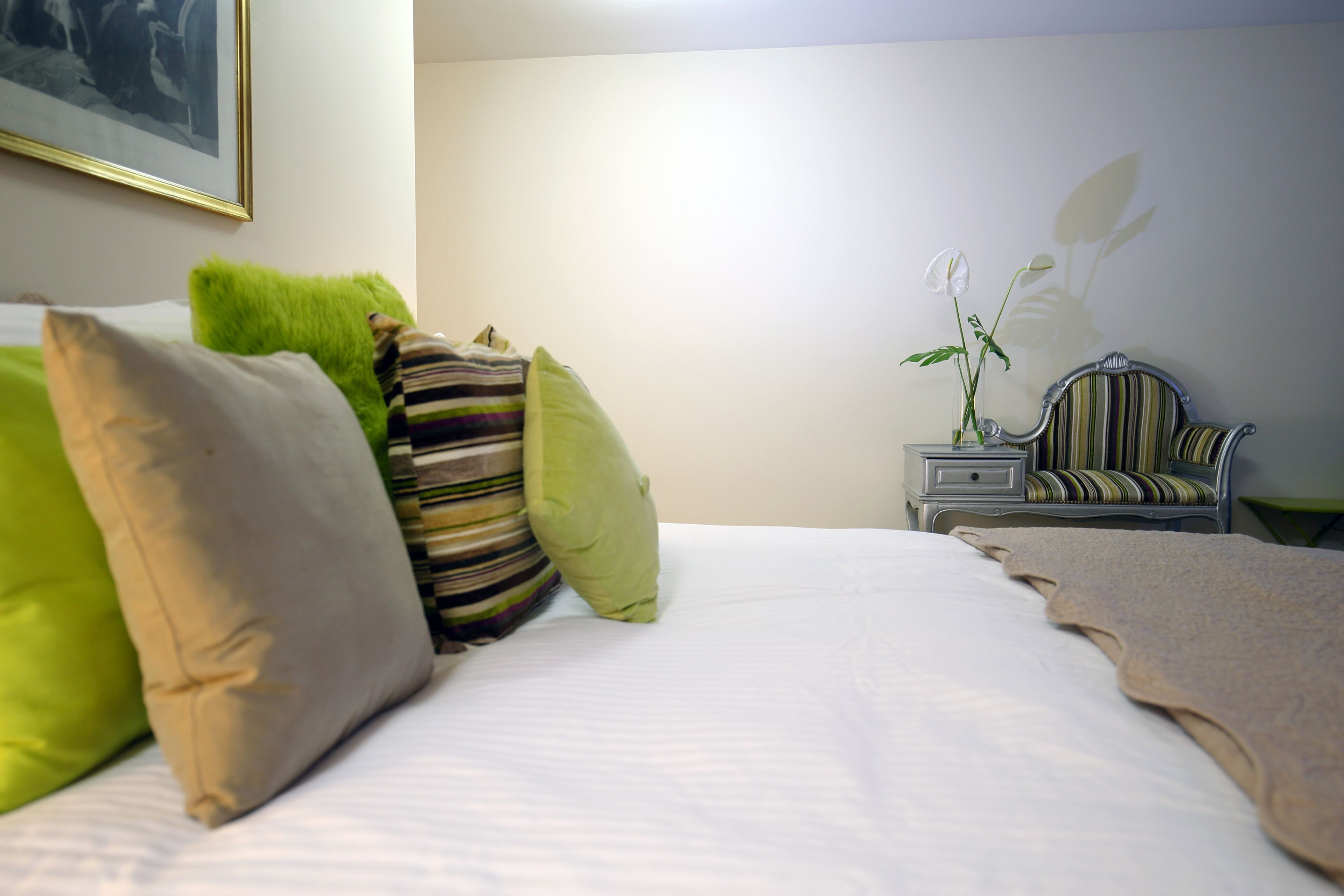 Una cama bien hecha con varias almohadas, una mesita de noche con un florero y una silla a rayas.