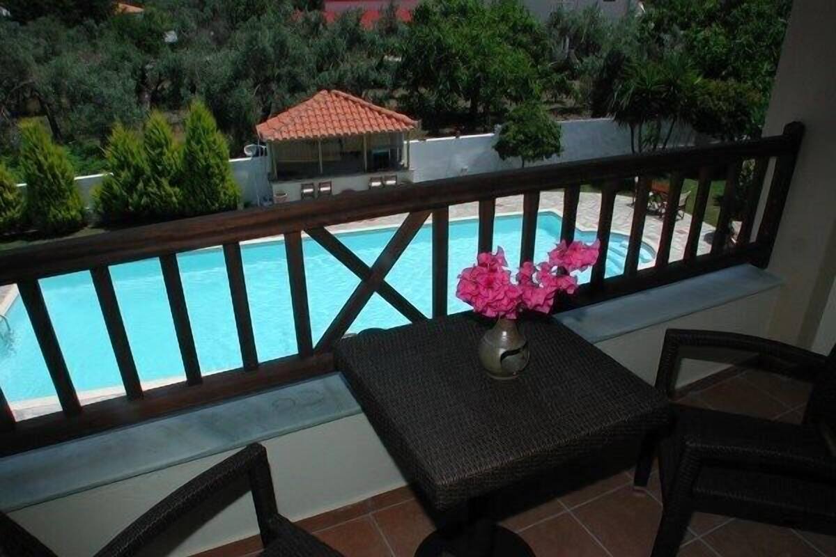 A balcony with a view of a swimming pool, a table with chairs, and a vase with flowers.