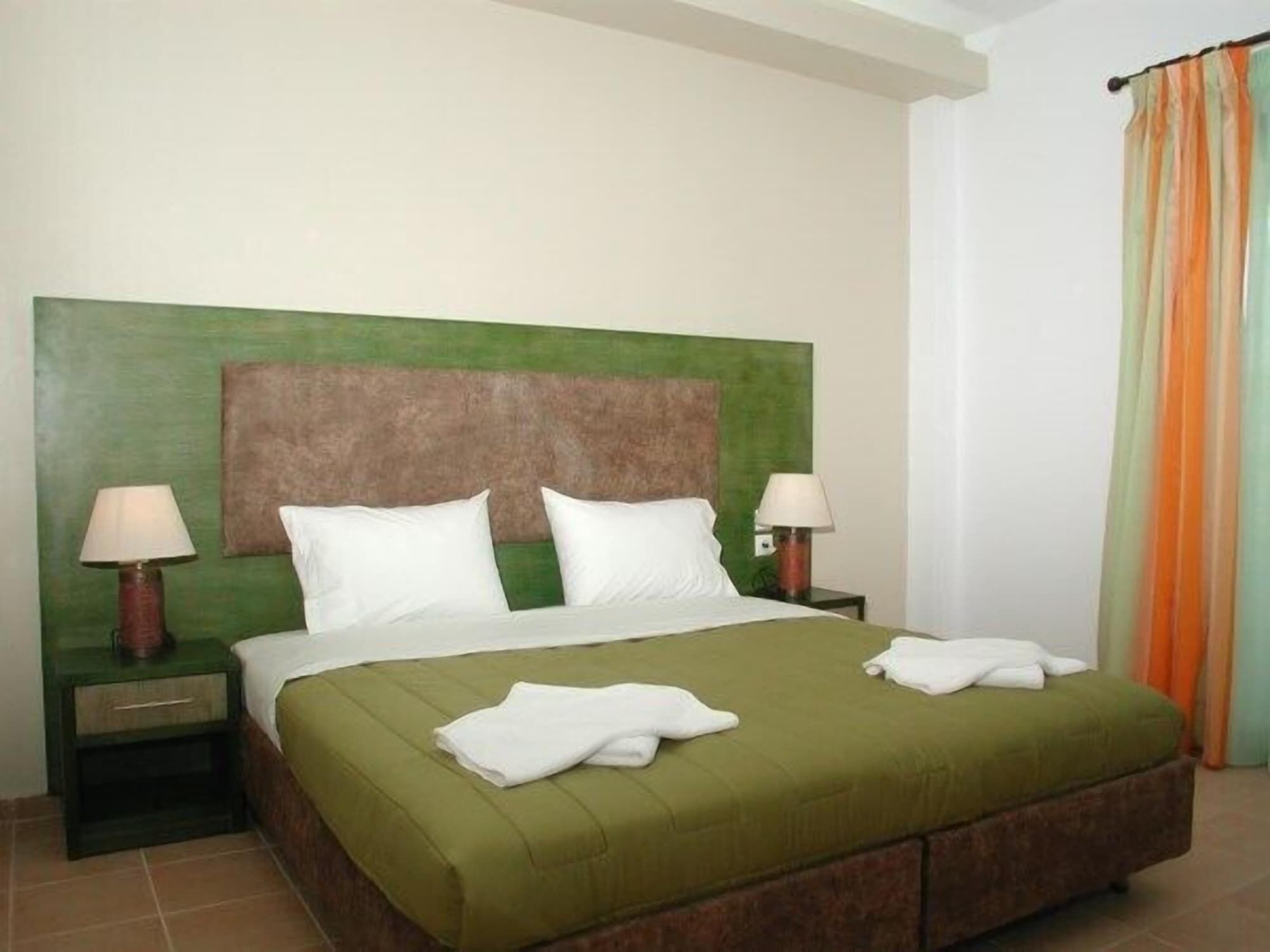 Habitación de hotel con una cama tapizada de verde, dos mesitas de noche con lámparas y un cabecero con diseño texturizado.
