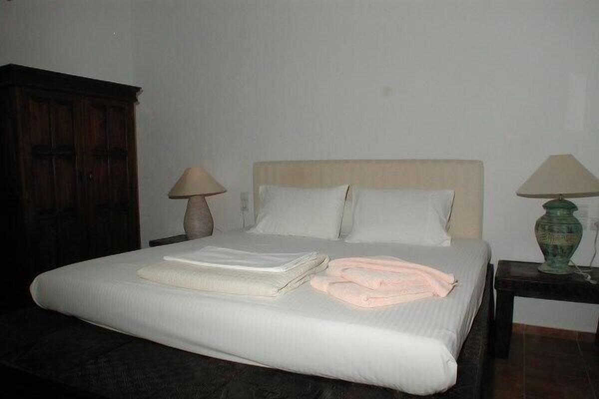 A neatly made bed with pillows and folded towels, a wooden wardrobe, and two bedside lamps on either side.