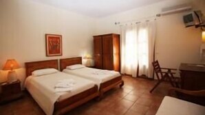 Una camera d'albergo con due letti, un armadio in legno, una scrivania e una sedia.