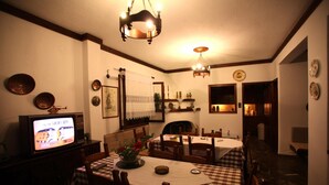 Un'area pranzo con tovaglia a quadri, sedie di legno, un televisore e piatti decorativi appesi al muro.