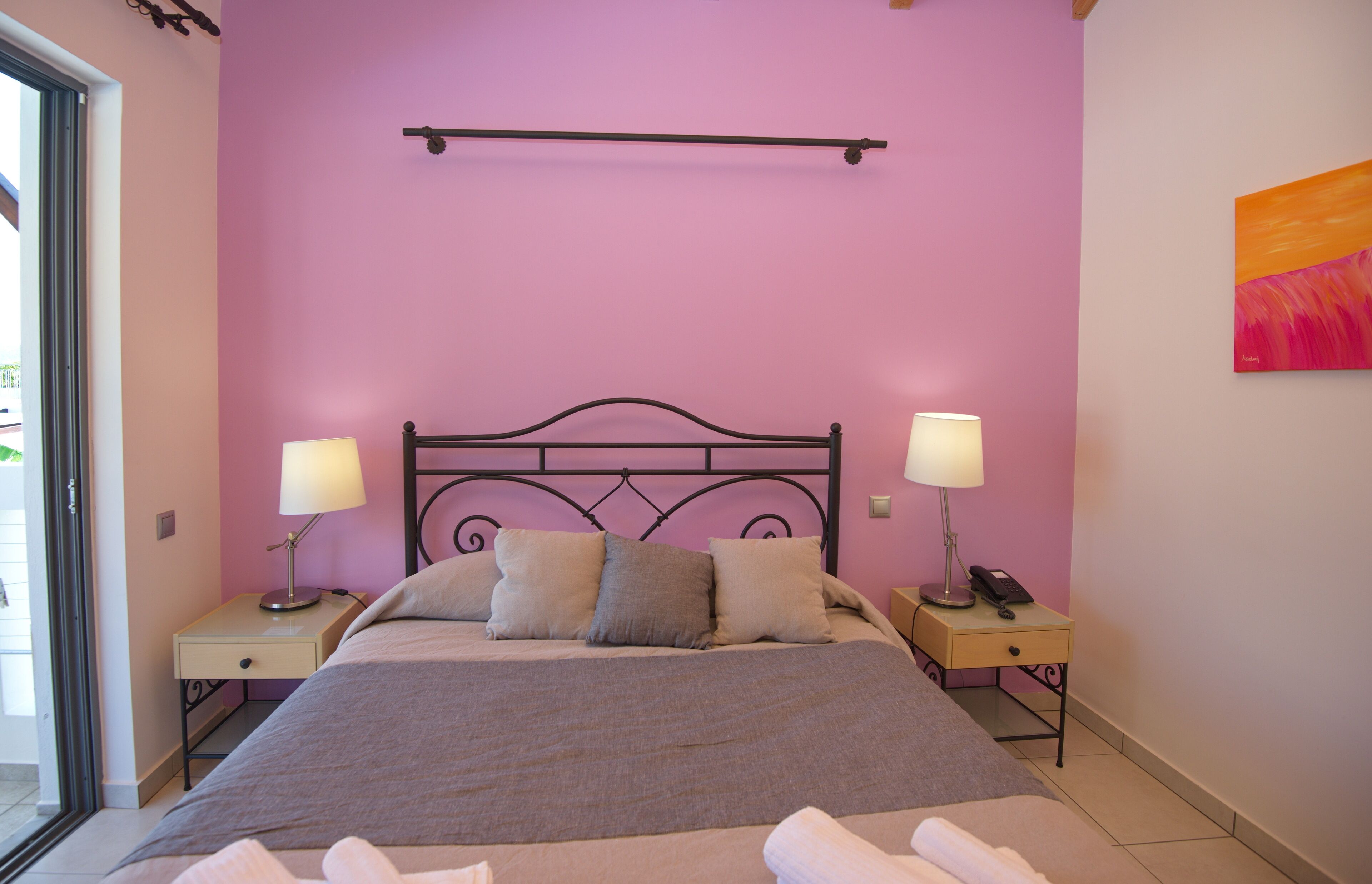 A bedroom with a bed, two bedside tables with lamps, a wall-mounted shelf, and a painting.