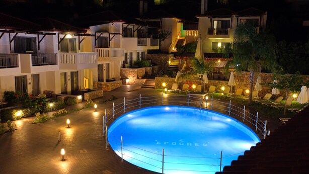 Ein Swimmingpool mit umlaufender Sonnenterrasse, eine Treppe, die zu einer zweiten Etage führt, und ein gut beleuchteter Außenbereich mit Liegestühlen und Sonnenschirmen.