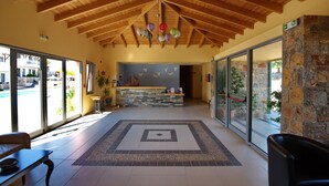 Eine großzügige Lobby mit hoher Holzbalkendecke, einem Empfangsbereich und großen Glasüren, die nach draußen führen.