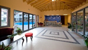 Eine geräumige Lobby mit Holzbalkendecke, einer Rezeption und Blick auf einen Pool.