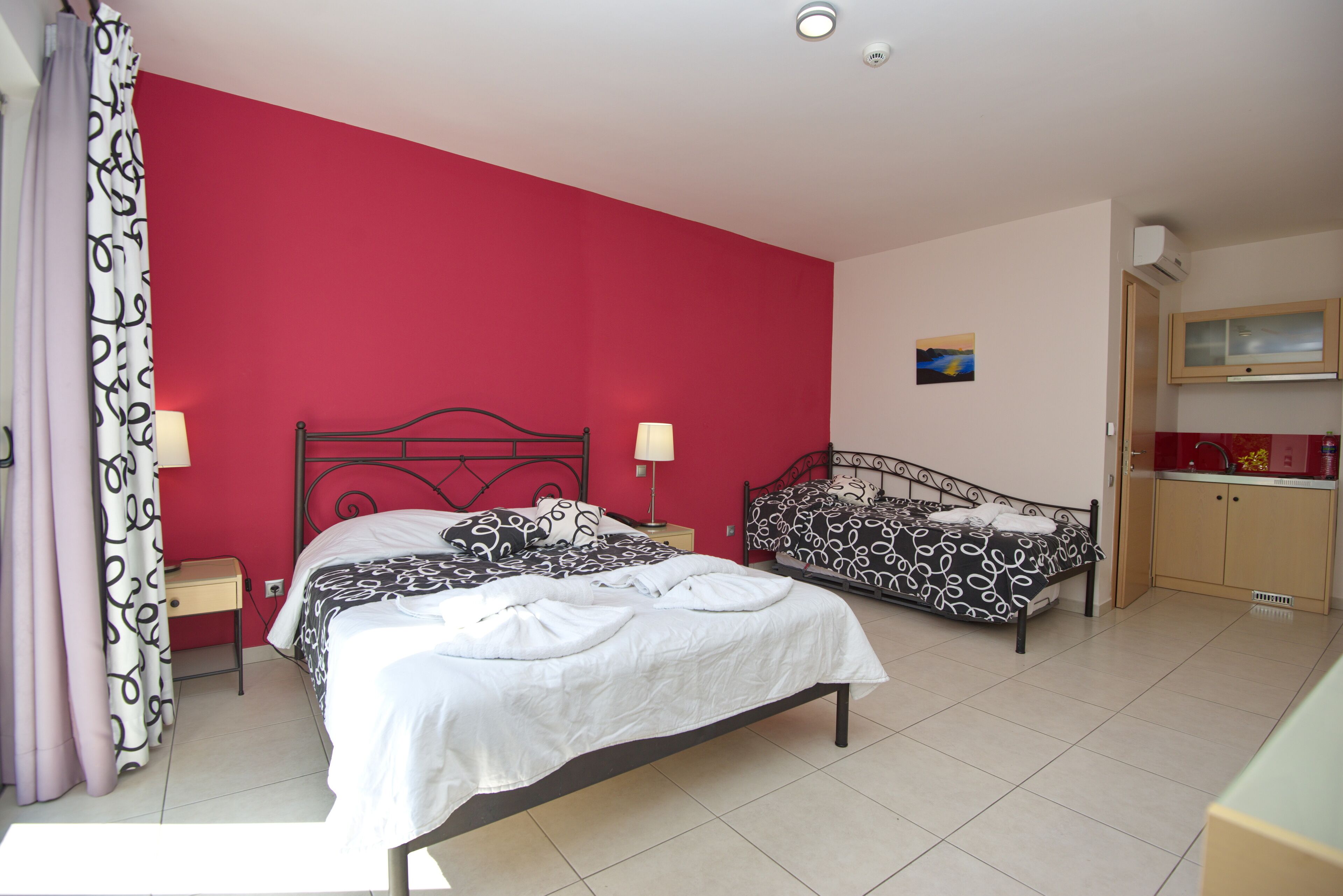 Un dormitorio con dos camas, una pared roja, una pequeña cocina y una ventana.