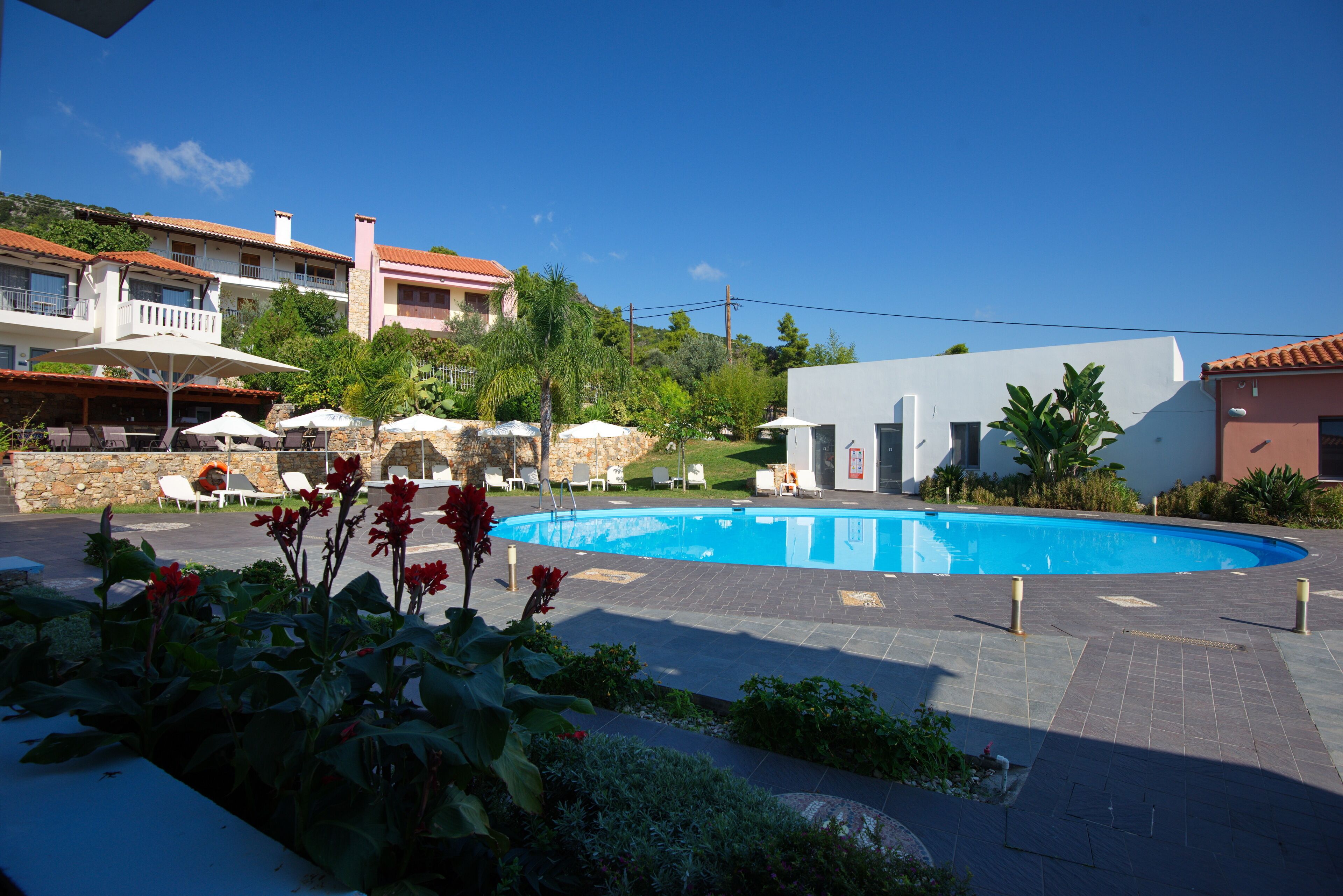 Ein Poolbereich mit Liegestühlen und Sonnenschirmen, umgeben von Gebäuden mit Balkonen und einem strahlend blauen Himmel.