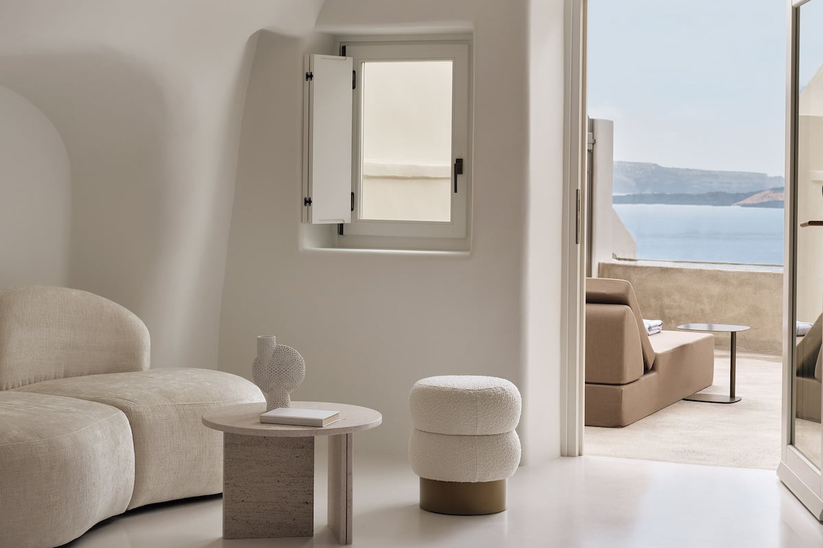 A minimalist room with a curved ceiling, a large window, a sofa, a small table, and an ottoman.
