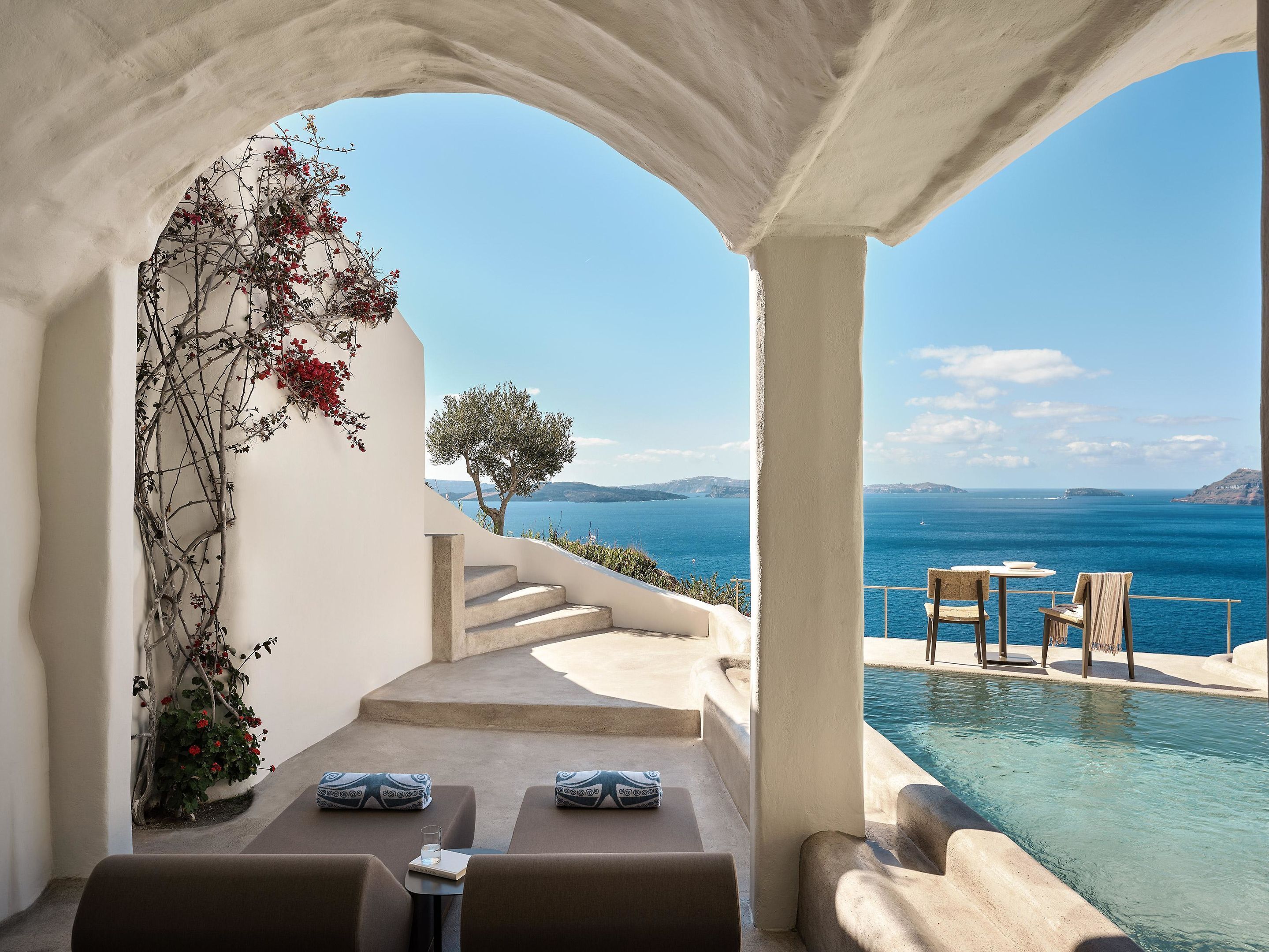 A poolside area with two lounge chairs, a small table, and a view of the sea.